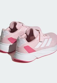 Scarpe sportive rosa con tessuto testurizzato, strisce bianche, cinturino a strappo e suola bianca con accenti rosa.