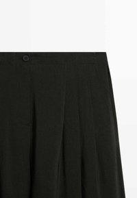 Schwarze, hochtaillierte Hose mit vorderen Falten, Seitentaschen und einem einzelnen schwarzen Knopf am Bund.