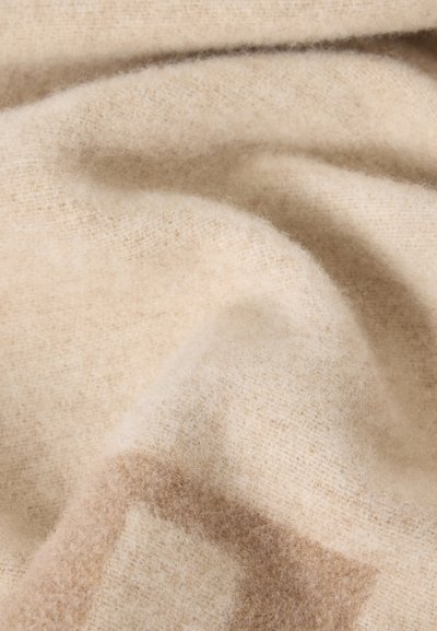 Tissu en laine beige doux avec une texture tissée subtile et de légers plis d'ombre créant une apparence chaleureuse et confortable.