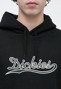 Μαύρο φούτερ με κορδόνια, με λευκή κεντημένη επιγραφή "Dickies" στο στήθος. Το υλικό φαίνεται απαλό με ομαλή υφή.