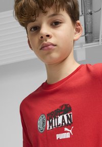 Červené bavlnené tričko s nápisom "FORZA MILAN" a logom AC Milan. Krátke rukávy s zaobleným výstrihom, na spodnej strane potlačené logo Puma.