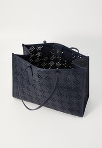 Sötétkék vászontáska perforált anyagból, geometrikus mintával, két fogantyúval és gombos záródással. A belső tér tágas.