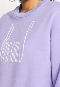 Lila sweatshirt med en mjuk textur, prydd med en stor vit grafisk texttryck på framsidan och en klassisk rund halsringning.