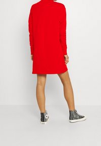 Vestido sudadera rojo con mangas largas y un cuello alto, combinado con zapatillas de deporte de patrón blanco y negro. Textura suave, diseño hasta la rodilla.