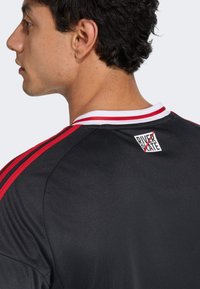 Camisa atlética negra con rayas rojas y blancas en las mangas y el cuello. Presenta una etiqueta en la parte posterior con un logo que dice "RIVER PLATE."