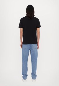 Svart kortärmad t-shirt i kombination med ljusblå raka jeans, med klassisk denimstil och detaljer på bakfickorna.