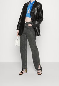 Blazer oversize en simili cuir crocodile noir, top bleu court, jean gris à jambes larges avec fentes latérales, et sandales noires à talons avec lanières.