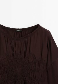Blouse marron foncé avec col rond et motif de broderie texturée détaillé au centre devant, étiquetée Massimo Dutti.