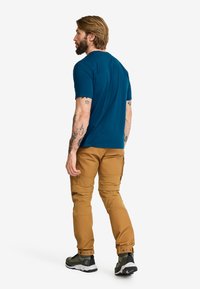 Herrblå skjorta, bruna cargobyxor med fickor, och svarta och gröna sneakers. Tyget är slätt, passformen är åtsittande, synliga sömmar och tryckknappar vid byxornas nederkant.