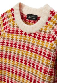 Pull en tricot avec un design à côtes de motifs blancs, rouges, jaunes et bruns. Encolure ronde avec une texture douce. Étiquette de marque visible.