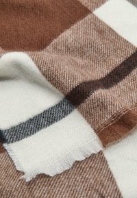 Écharpe à carreaux marron et crème, fabriquée en tissu tissé doux. Présente des bords à franges et une surface texturée avec des nuances de marron variées.