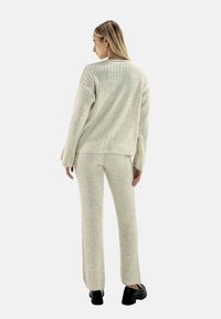 Beżowy sweter z prążkowanego materiału oraz pasujące do niego spodnie, charakteryzujące się luźnym krojem i długimi rękawami, uzupełnione czarnym obuwiem.