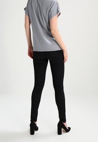 Grå kortärmad topp med mönstrad halsringning, kombinerad med slim-fit svarta byxor och svarta högklackade skor. Slät tygstruktur.