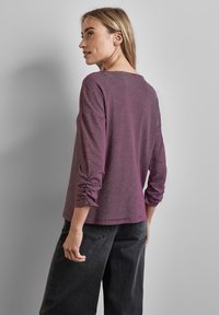Lange mouwen, paarse gestreepte blouse met een geplooid detail bij de manchetten; gecombineerd met zwarte broek. Zachte stof met een casual pasvorm.