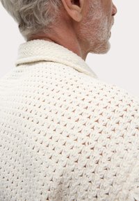 Cardigan en laine crème, mettant en avant un motif texturé avec un col. Vu de dos, mettant en valeur le tissage ouvert et le tissu doux.