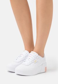 Baskets plateformes blanches avec un design perforé, des lacets plats et une semelle texturée. Rehaussées de détails en rose clair et en or.