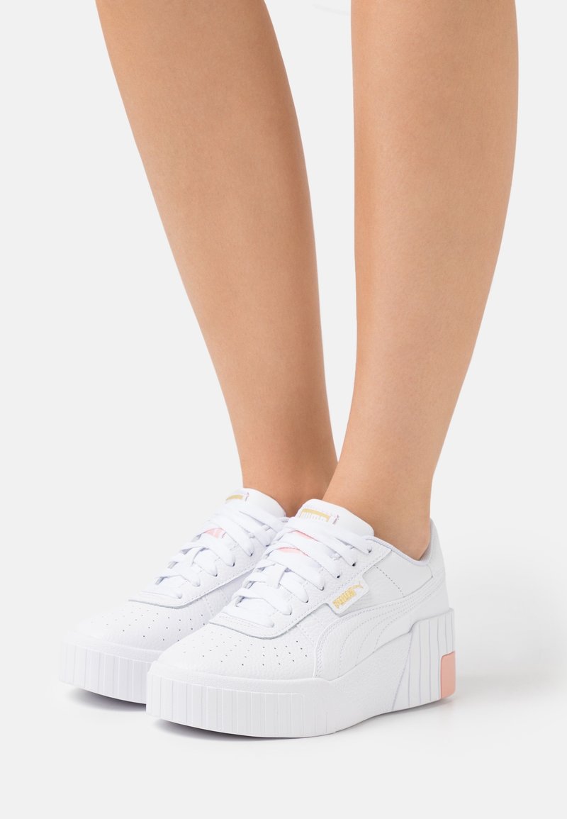 Baskets plateformes blanches avec un design perforé, des lacets plats et une semelle texturée. Rehaussées de détails en rose clair et en or.