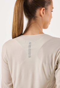 Lichtbeige shirt met lange mouwen van gestructureerde stof, met een verticale "SWEDEMOUNT"-logo aan de achterkant en een subtiel ruitpatroon.