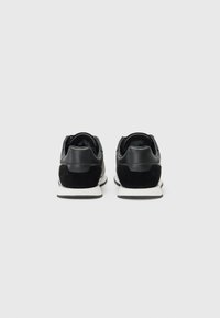 Zwarte sneakers van suède en gestructureerd leer, met een witte zool en een gevoerde kraag. Standaard vetersluiting en minimalistisch ontwerp.