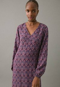 Rochie violet cu mâneci lungi, de tip V, cu un model ondulat și pliseuri. Materialul pare ușor și texturat, având mâneci elasticizate.
