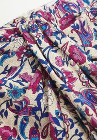 Tissu avec un fond beige présentant des plis et un motif floral dans des tons de rose, bleu et violet.