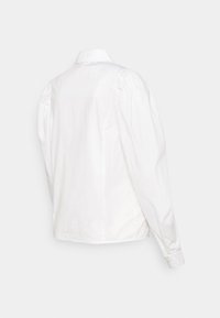 Blusa de algodão branca, com decote de gola e mangas bufantes. A parte de trás é lisa, com bainha reta e punhos com botões.