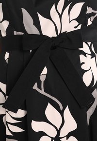 Tessuto a fiori in bianco e nero con una ampia cintura nera annodata a fiocco in vita.