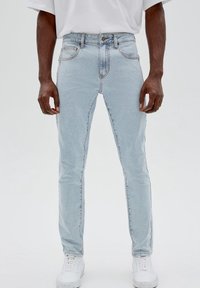 Ljust blå skinny jeans i denim, med hög midja, fem fickor, diskret sömnad och fransig fåll. I kombination med vita sneakers.