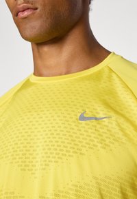 Camiseta de rendimiento amarilla con un patrón texturizado. Presenta un logo de Nike gris en el pecho. Cuello redondeado y mangas cortas.