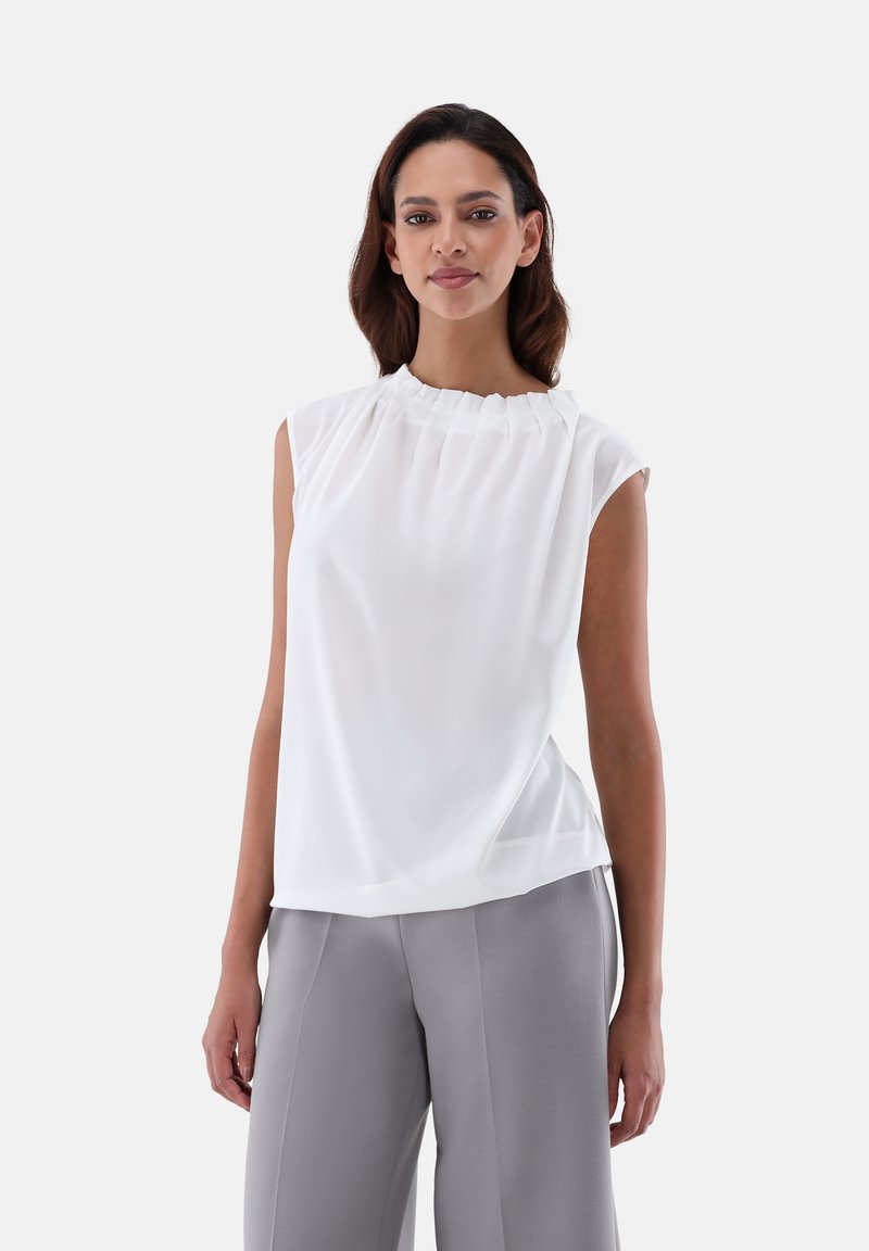Blusa bianca senza maniche con collo plissettato, realizzata in tessuto leggero, abbinata a pantaloni larghi grigi. Texture morbida, design semplice.