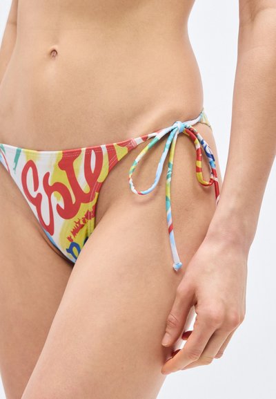 Κοντινό πλάνο του κάτω μέρους του σώματος ενός ατόμου που φοράει πολύχρωμο μπικίνι με κορδόνια στο πλάι και κόκκινα, κίτρινα, μπλε και λευκά σχέδια σε ανοιχτόχρωμο δέρμα.