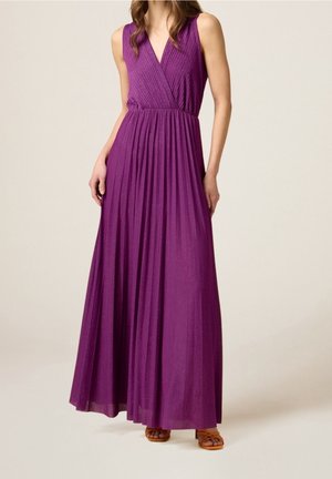 Robe maxi plissée violette sans manches avec un décolleté en V portée par une femme debout, assortie à des sandales marron à brides.
