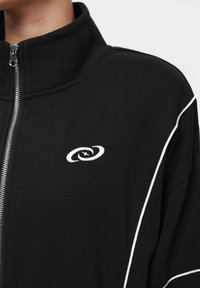 Black zip-up jacket with white piping along the shoulder and a small white embroidered swirl logo on the chest.