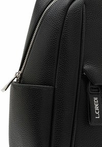 Black leather backpack featuring a textured surface, silver zipper, and a front pocket. Branding visible on the side tag.