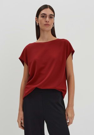 Rotes kurzärmliges Oberteil mit weitem Schiffs-Ausschnitt, aus weichem Material, mit drapierter Gestaltung und lockerer Passform, kombiniert mit schwarzen Hosen.