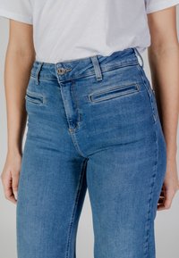 Pantalones vaqueros de mezclilla azul de cintura alta con una textura suave, dos bolsillos frontales y un cierre de botón metálico. Diseño clásico de pierna recta.