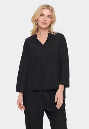 Maglietta nera a maniche lunghe con scollatura a V, forma rilassata e texture morbida; abbinata a pantaloni neri larghi, creando un look casual.