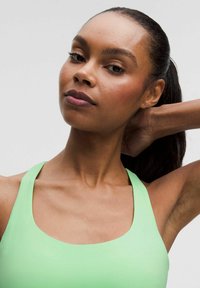 Jasnozielony top sportowy z szerokim dekoltem i cienkimi ramiączkami, wykonany z gładkiego materiału, prezentujący elegancki design i minimalne detale.