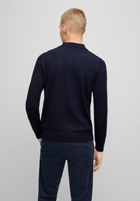 Marineblauer Pullover aus strukturiertem Strickstoff, mit langen Ärmeln und fittem Rippbund, kombiniert mit dunklen Hosen.