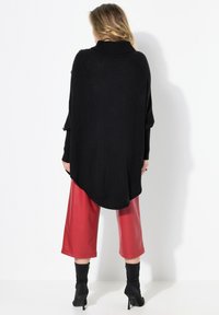 Pull noir oversize à col montant, associé à des culottes en simili cuir rouge vif et des bottes noires à talons montantes.