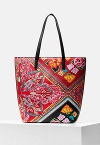 Sac fourre-tout en tissu rouge avec motifs floraux, poignées noires et accents géométriques. Présente une forme structurée avec des détails visuels vibrants.