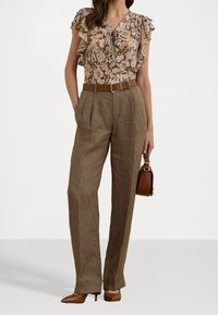 Blouse florale avec des manches volantes, pantalon à carreaux marron avec des plis, ceinture marron et un petit sac à main marron. Des chaussures à talons complètent le look.