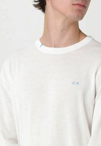 Camicia bianca a maniche lunghe in cotone con scollo rotondo, caratterizzata da un piccolo logo blu sul petto e un accento sul colletto.