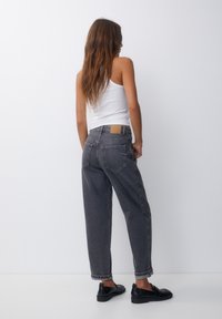 Grå högmidjade jeans med avslappnad passform, med subtil blekning, uppvikta fållar och en tan läderlapp på baksidan av midjebandet.