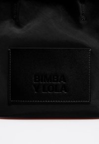 Borsa di stoffa nera con una toppa rettangolare in pelle testurizzata e il logo "BIMBA Y LOLA" impresso, accentuata da cuciture ordinate.