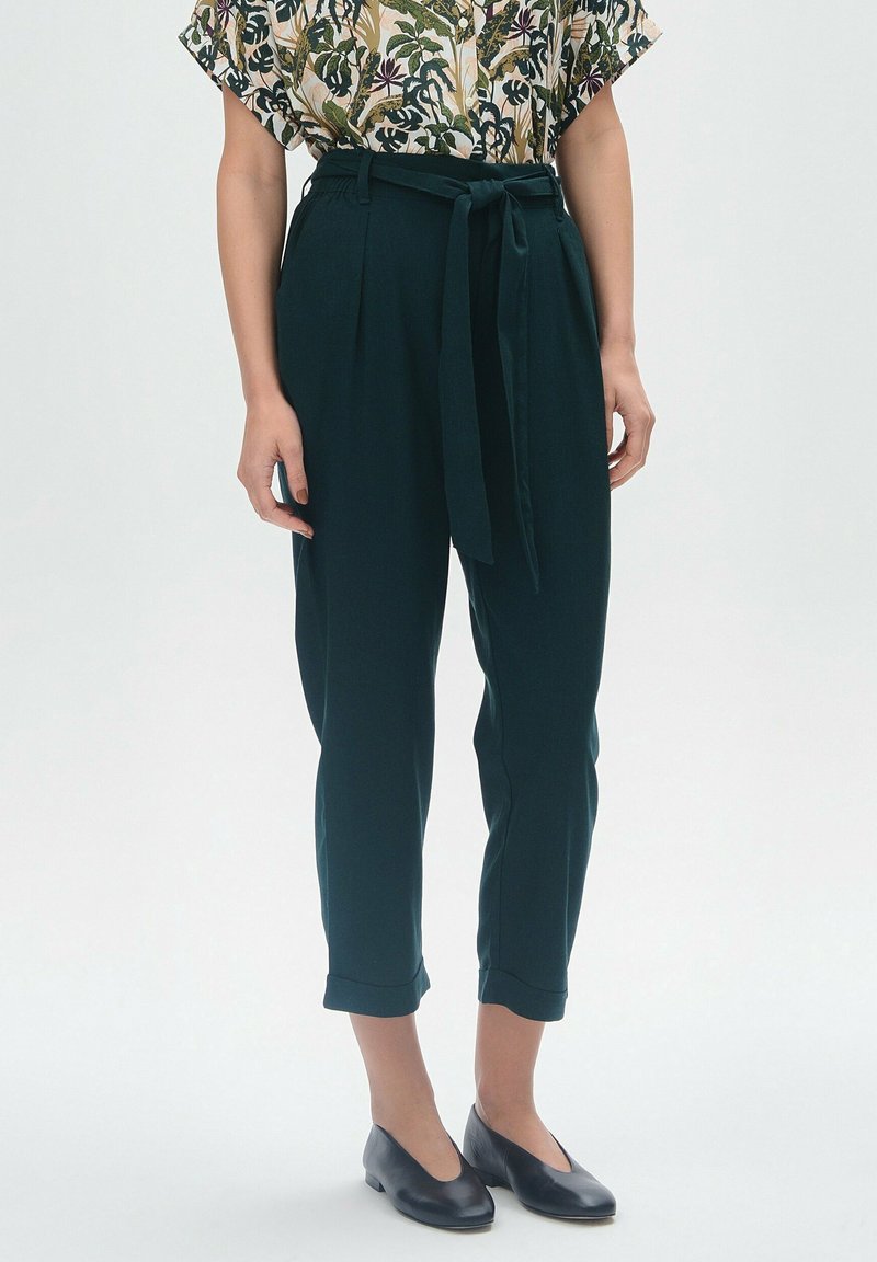 Ciemnozielone, wysokie spodnie z zawiązywanym paskiem, o skróconej długości i podwiniętych rękawach, wykonane z gładkiego, lekkiego materiału.