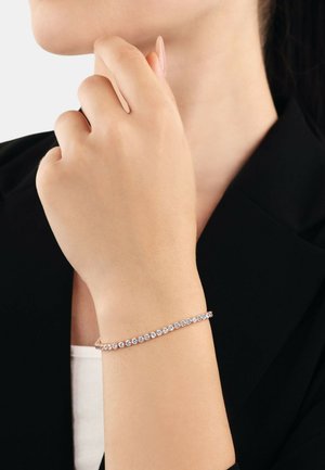 Bracciale in oro rosa con una fila di pietre preziose trasparenti che brillano, con un design delicato, appoggiato su un polso nudo.