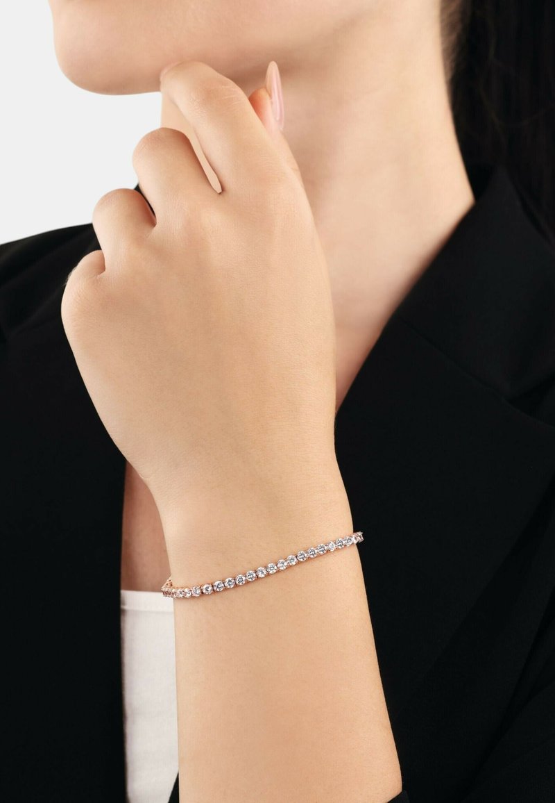 Armband aus Roségold, verziert mit einer Reihe von funkelnden, klaren Edelsteinen, in einem zarten Design, das auf einem nackten Handgelenk ruht.
