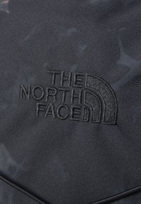 Black textured fabric featuring an embossed logo of The North Face in a curved design, with a subtle tonal pattern in the background.