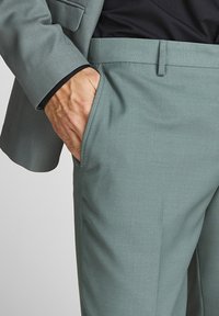 Pantaloni da uomo su misura di colore teal chiaro, realizzati in un tessuto morbido, a vestibilità slim, con tasche laterali e un design pulito e minimalista.